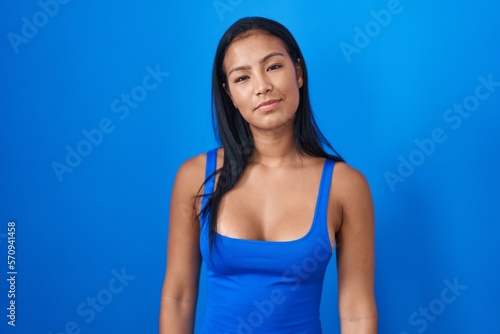 Hispanic woman standing over blue background relaxed with serious expression on face. simple and natural looking at the camera. © Krakenimages.com