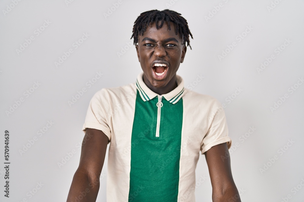 African man with dreadlocks standing over isolated background angry and mad screaming frustrated and furious, shouting with anger. rage and aggressive concept. African man with dreadlocks standing over isolated background angry and mad screaming frustrated and furious, shouting with anger. rage and aggressive concept.