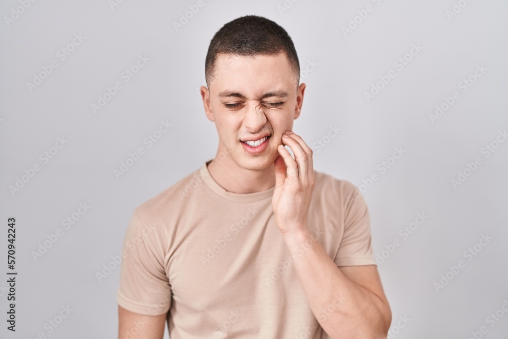 Young man standing over isolated background touching mouth with hand with painful expression because of toothache or dental illness on teeth. dentist Young man standing over isolated background touching mouth with hand with painful expression because of toothache or dental illness on teeth. dentist