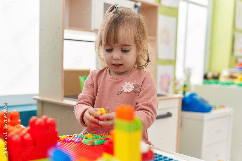 Adorable blonde girl playing with construction blocks standing at kindergarten Adorable blonde girl playing with construction blocks standing at kindergarten