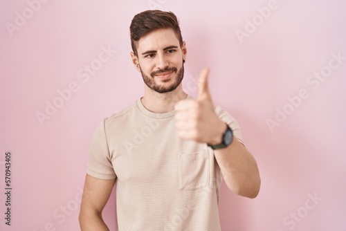 Hispanic man with beard standing over pink background looking proud, smiling doing thumbs up gesture to the side © Krakenimages.com