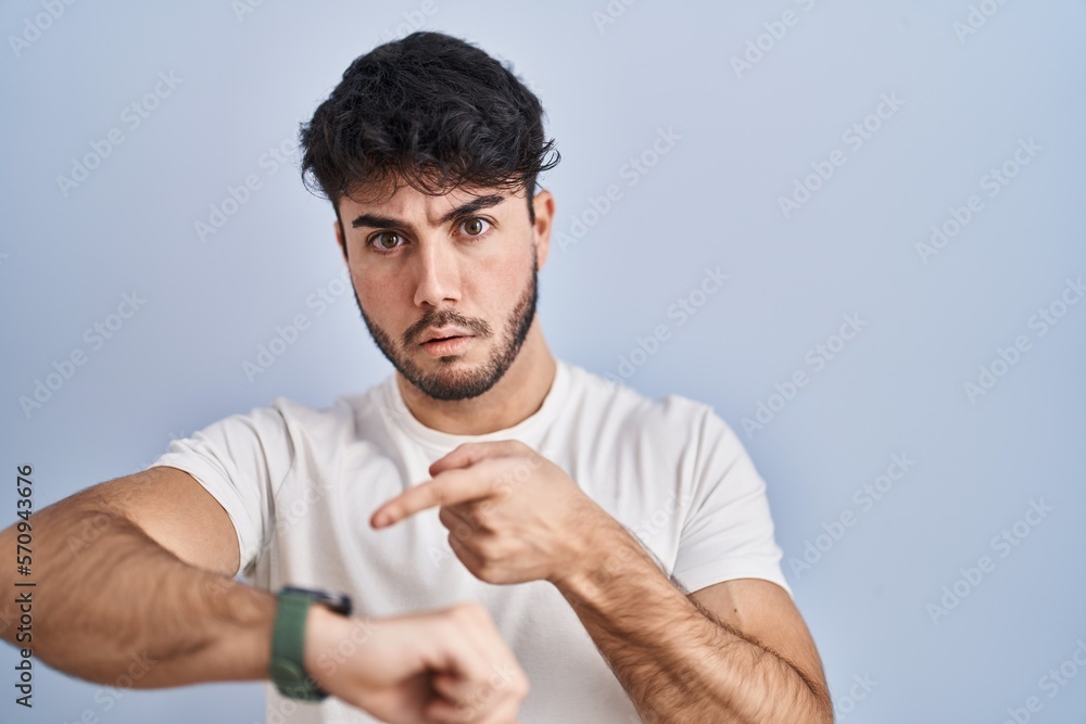 Hispanic man with beard standing over white background in hurry pointing to watch time, impatience, upset and angry for deadline delay Hispanic man with beard standing over white background in hurry pointing to watch time, impatience, upset and angry for deadline delay