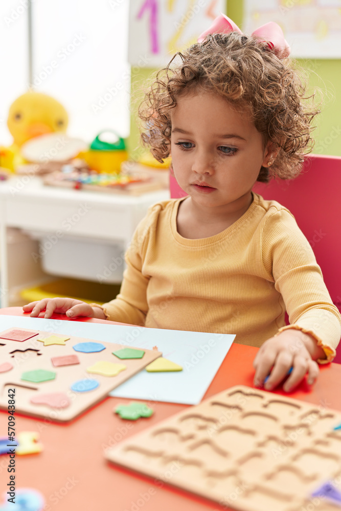 Adorable hispanic toddler playing with maths puzzle game sitting on table at kindergarten Adorable hispanic toddler playing with maths puzzle game sitting on table at kindergarten