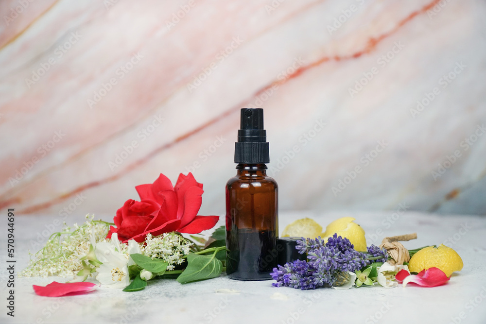 Floral face and body mist in amber spray bottle with lavender, rose, lemon, jasmine and elderflowers on marble background. Floral face and body mist in amber spray bottle with lavender, rose, lemon, jasmine and elderflowers on marble background.