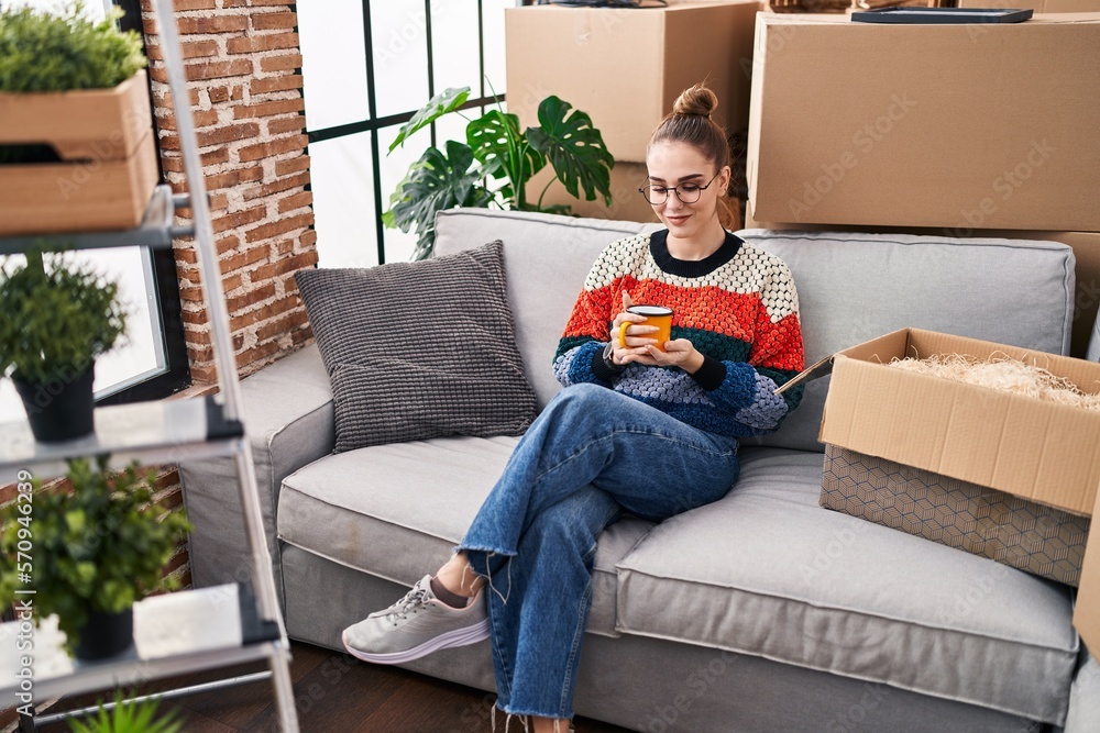Young woman drinking coffee sitting on sofa at new home