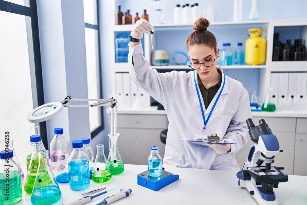 Young woman scientist reading document measuring liquid at laboratory Young woman scientist reading document measuring liquid at laboratory