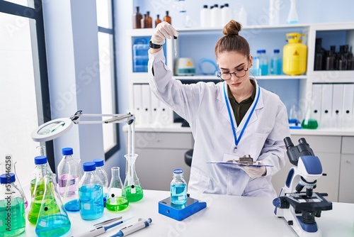 Young woman scientist reading document measuring liquid at laboratory