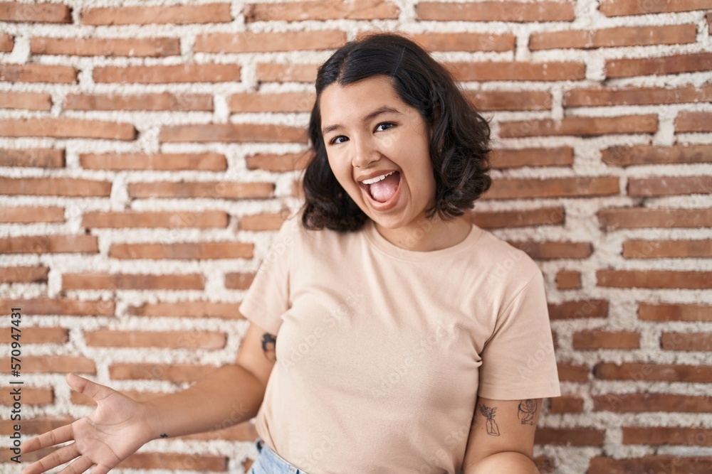 Young hispanic woman standing over bricks wall smiling cheerful with open arms as friendly welcome, positive and confident greetings Young hispanic woman standing over bricks wall smiling cheerful with open arms as friendly welcome, positive and confident greetings