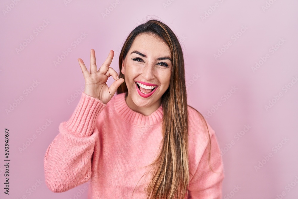 Young hispanic woman standing over pink background smiling positive doing ok sign with hand and fingers. successful expression. Young hispanic woman standing over pink background smiling positive doing ok sign with hand and fingers. successful expression.