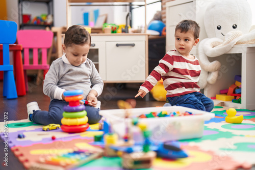 Two kids playing with toys sitting on floor at kindergarten