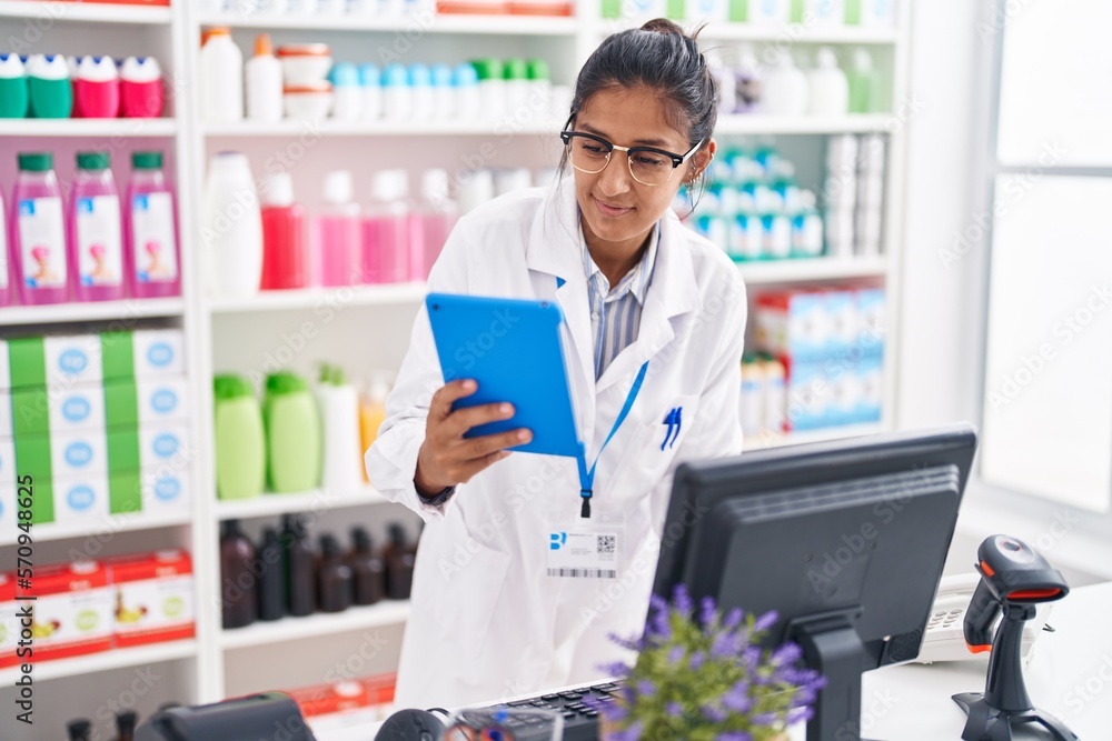 Young beautiful hispanic woman pharmacist using touchpad and computer working at pharmacy