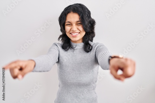 Hispanic woman with dark hair standing over isolated background pointing to you and the camera with fingers, smiling positive and cheerful