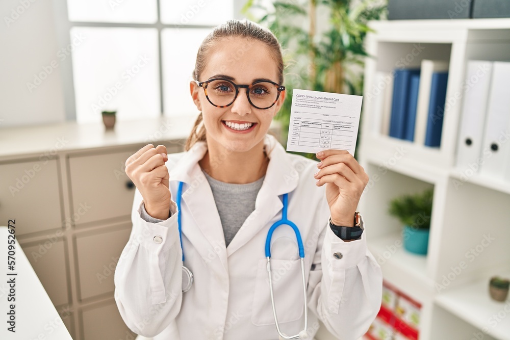 Young doctor woman holding covid certificate screaming proud, celebrating victory and success very excited with raised arm Young doctor woman holding covid certificate screaming proud, celebrating victory and success very excited with raised arm