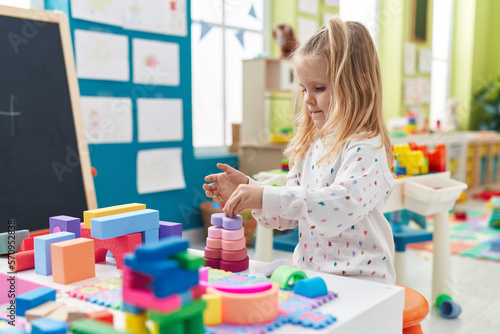 Adorable blonde girl playing with construction blocks standing at kindergarten