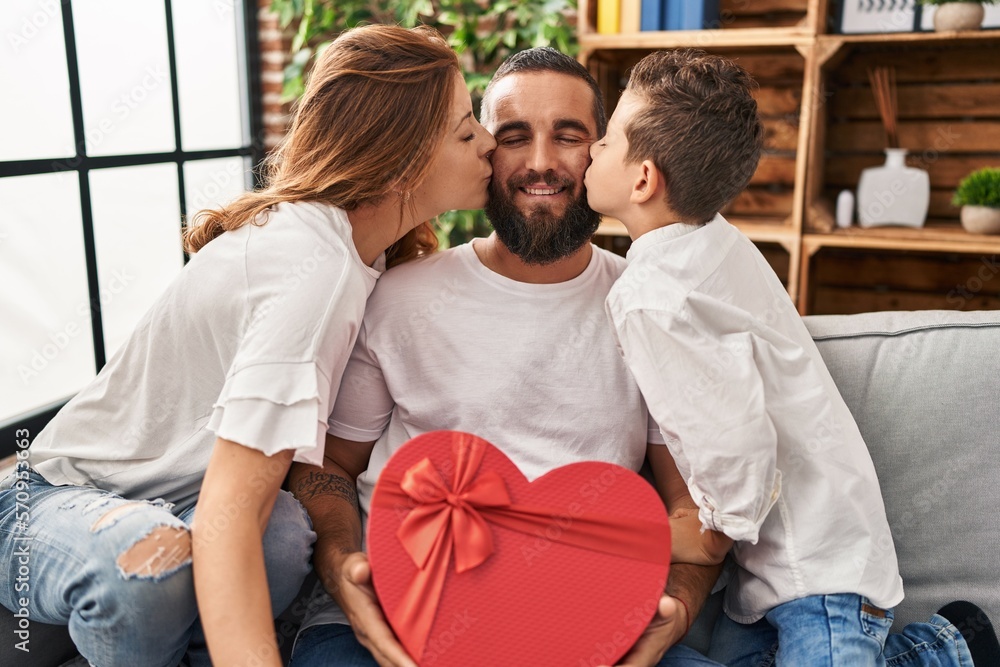 Obraz premium Family kissing father holding heart box gift at home