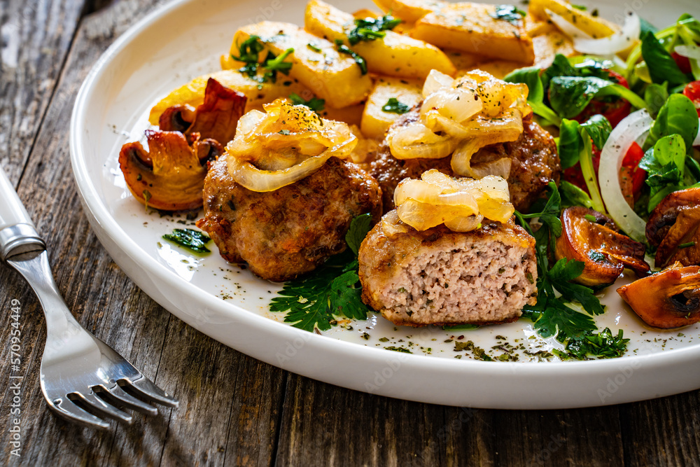 Fried pork meatballs with fried onion, french fries and fresh vegetables on wooden table
Fried pork meatballs with fried onion, french fries and fresh vegetables on wooden table