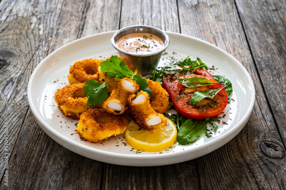 Fried breaded calamari rings with lemon and fresh vegetables on wooden table
