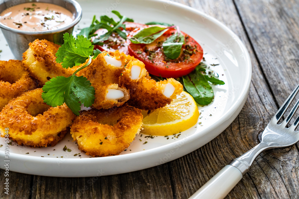 Fried breaded calamari rings with lemon and fresh vegetables on wooden table
Fried breaded calamari rings with lemon and fresh vegetables on wooden table
