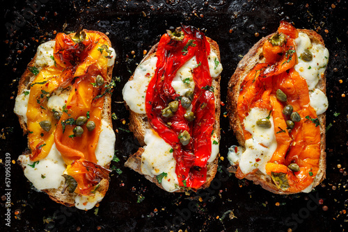 Grilled sandwiches with peppers and mozzarella cheese, sprinkled with aromatic herbs on a black background