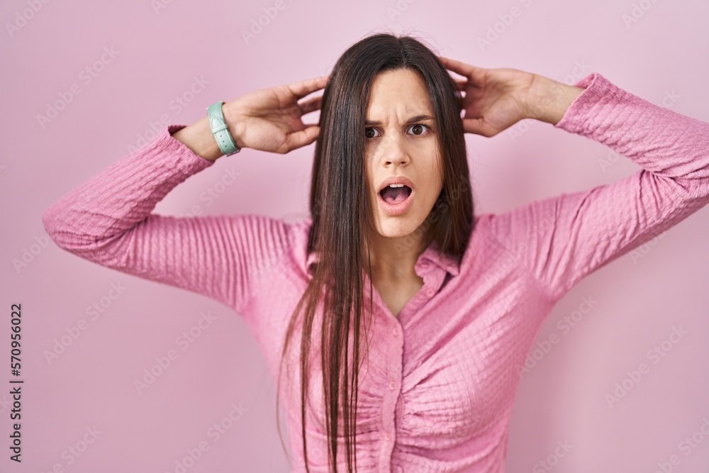 Young hispanic woman standing over pink background crazy and scared with hands on head, afraid and surprised of shock with open mouth Young hispanic woman standing over pink background crazy and scared with hands on head, afraid and surprised of shock with open mouth
