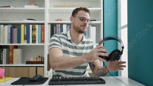 Young caucasian man using computer wearing headphones at library university