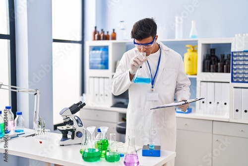 Young hispanic man scientist smelling liquid on test tube at laboratory