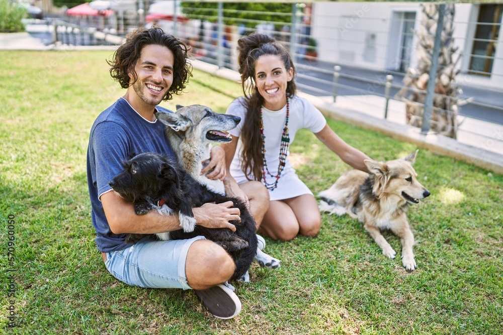 Man and woman couple smiling confident sitting on herb with dogs at park Man and woman couple smiling confident sitting on herb with dogs at park