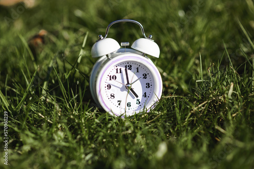 White color alarm clock on green grass. Time, circadian rhythm, early rise concept.