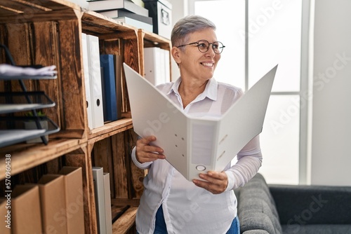 Middle age woman psychologist reading binder standing at pyschology center photo