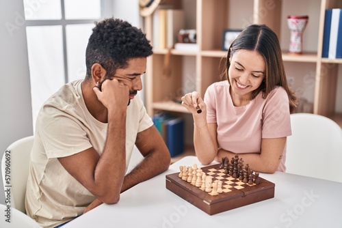 Man and woman couple sitting on table playing chess at home