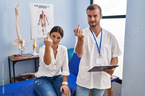 Young hispanic woman at physiotherapist appointment showing middle finger  impolite and rude fuck off expression