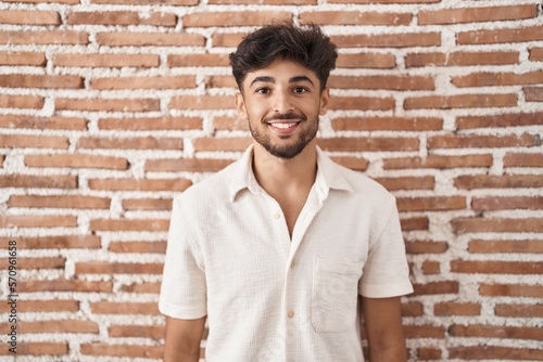 Arab man with beard standing over bricks wall background with a happy and cool smile on face. lucky person.