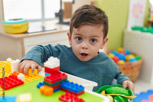 Adorable hispanic boy playing with construction blocks sitting on table at kindergarten