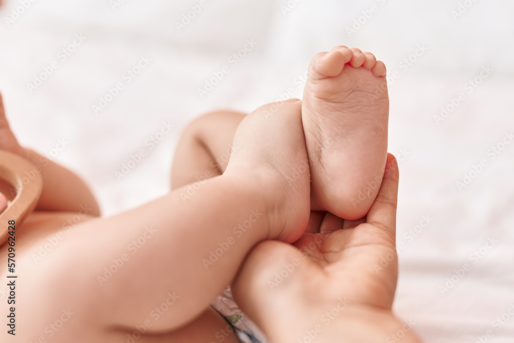 Adorable hispanic toddler lying on bed having feet massage at bedroom Adorable hispanic toddler lying on bed having feet massage at bedroom