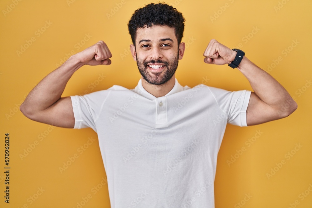 Arab man standing over yellow background showing arms muscles smiling proud. fitness concept. Arab man standing over yellow background showing arms muscles smiling proud. fitness concept.