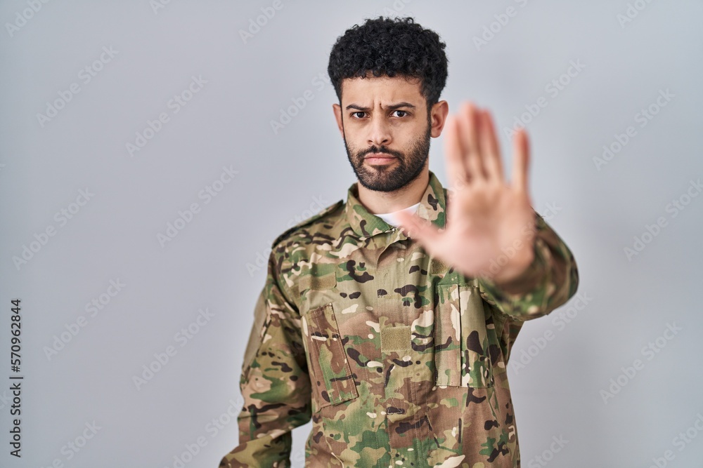Arab man wearing camouflage army uniform doing stop sing with palm of the hand. warning expression with negative and serious gesture on the face.
