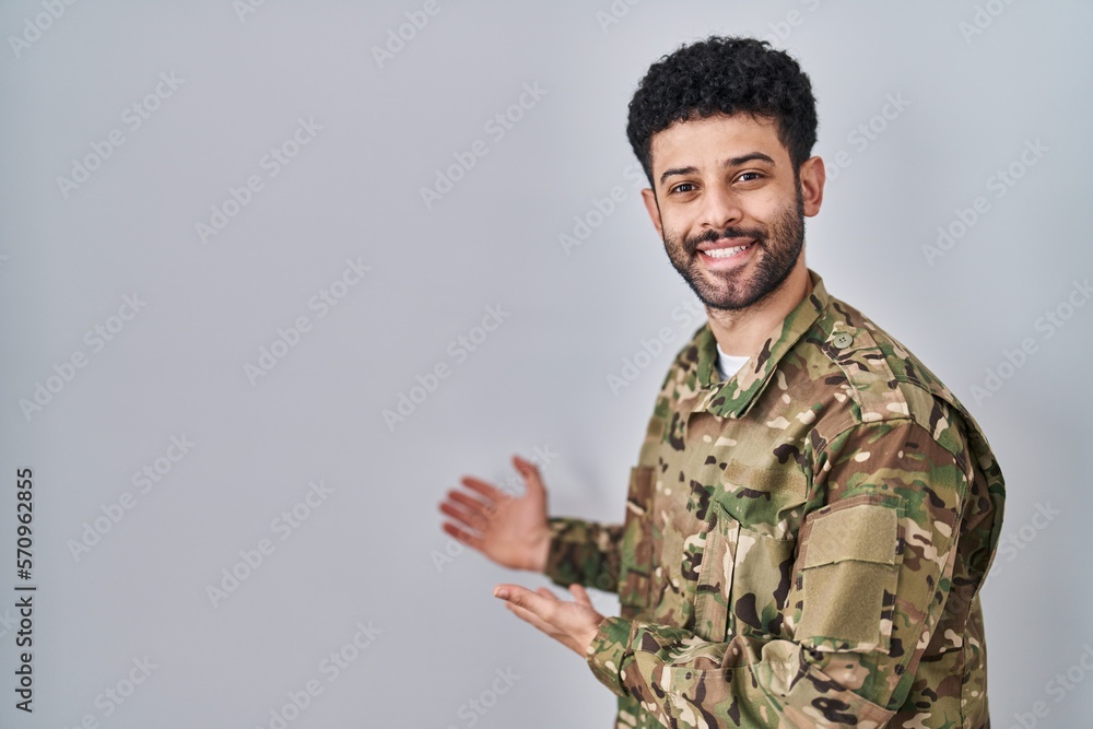 Arab man wearing camouflage army uniform inviting to enter smiling natural with open hand