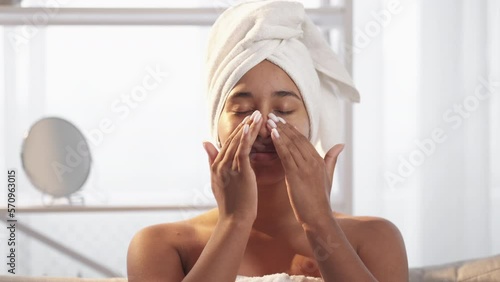 Skin moisturizing. Facial skincare. Beauty routine. Satisfied relaxed smiling woman applying nourishing face cream after morning shower in light bathroom with free space.