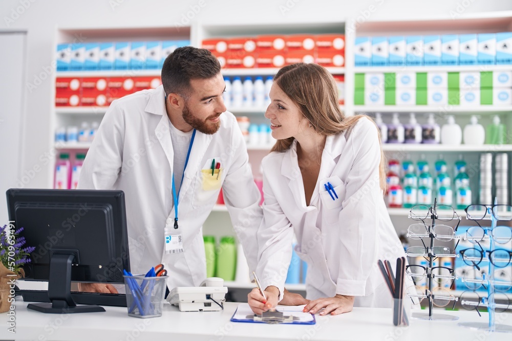 Man and woman pharmacists smiling confident writing on document at pharmacy