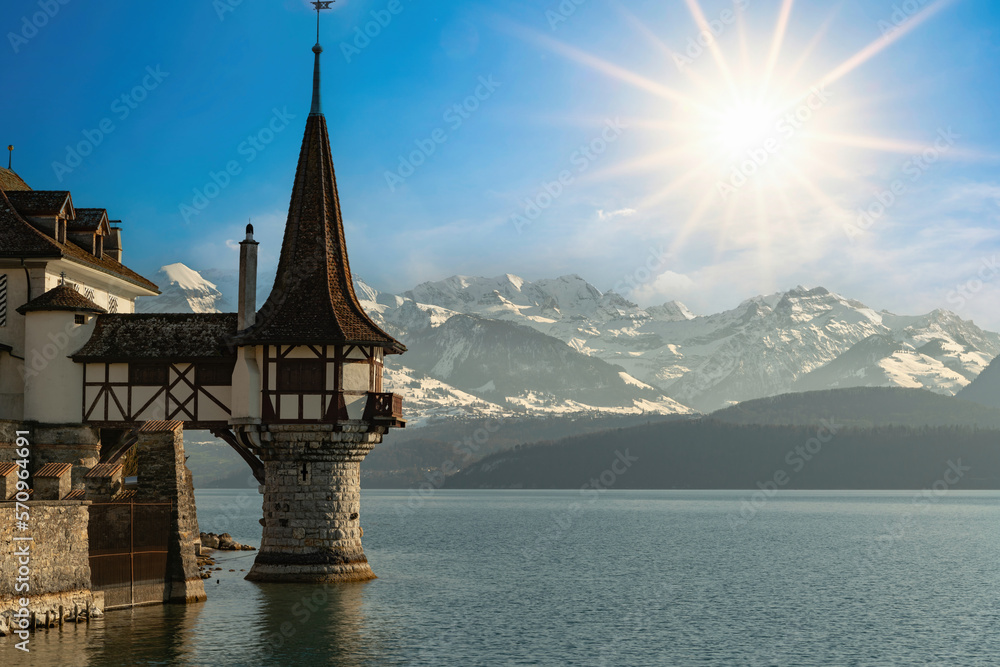 Scenic view of amazing Oberhofen castle of Lake Thun and illuminated by sunlight. Snowcapped mountains and picturesque sky on background, Switzerland