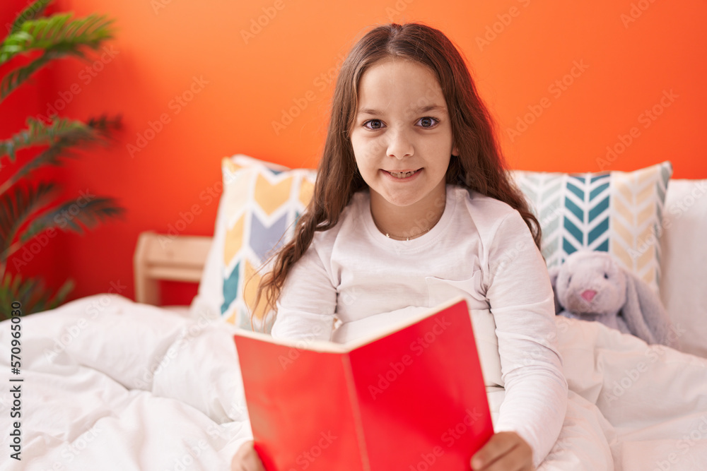 Adorable hispanic girl reading book sitting on bed at bedroom Adorable hispanic girl reading book sitting on bed at bedroom