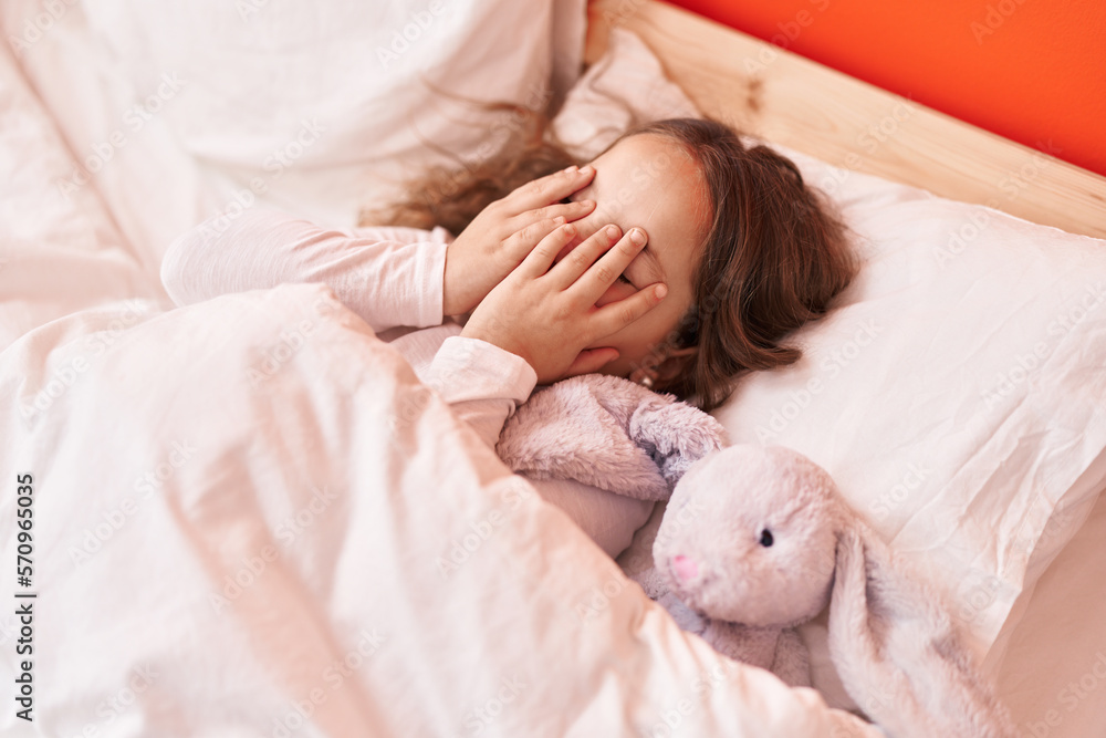Obraz premium Adorable hispanic girl covering eyes lying on bed at bedroom
