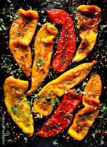 Grilled peppers of different colors cut in half sprinkled with herbs on a black background, top view