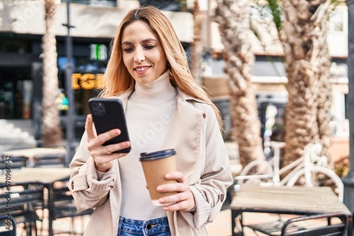 Young blonde woman using smartphone drinking coffee at coffee shop terrace
