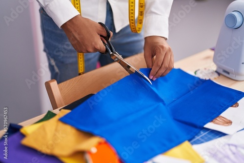Young hispanic teenager tailor cutting cloth at tailor shop