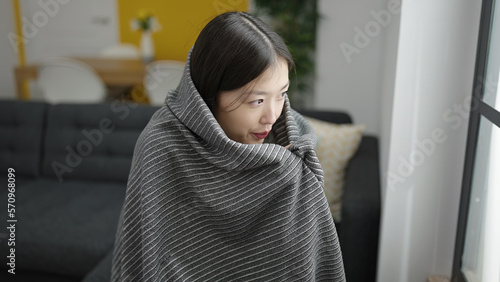 Young chinese woman covering with blanket for cold sitting on sofa at home