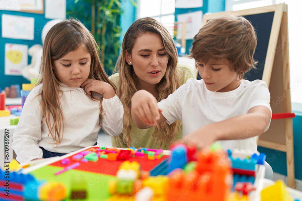 Teacher with boy and girl playing with construction blocks sitting on table at kindergarten Teacher with boy and girl playing with construction blocks sitting on table at kindergarten