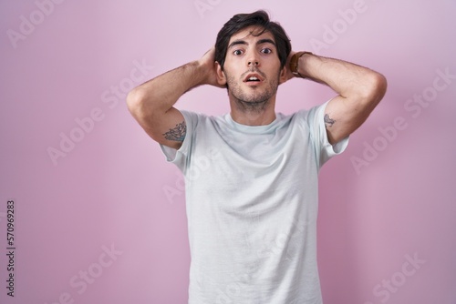 Young hispanic man standing over pink background crazy and scared with hands on head, afraid and surprised of shock with open mouth