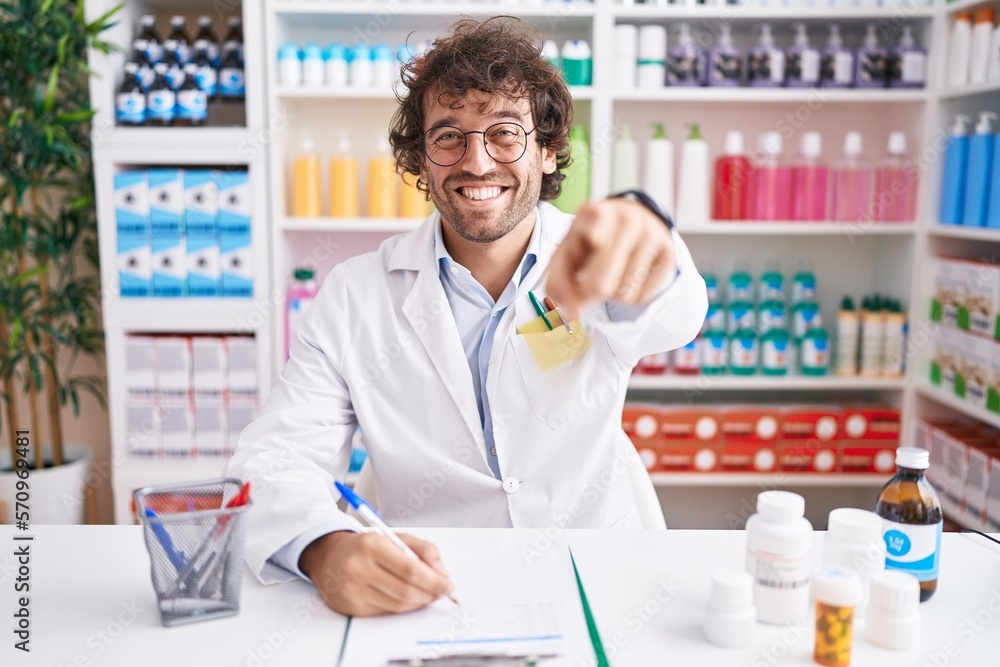 Hispanic young man working at pharmacy drugstore pointing to you and the camera with fingers, smiling positive and cheerful