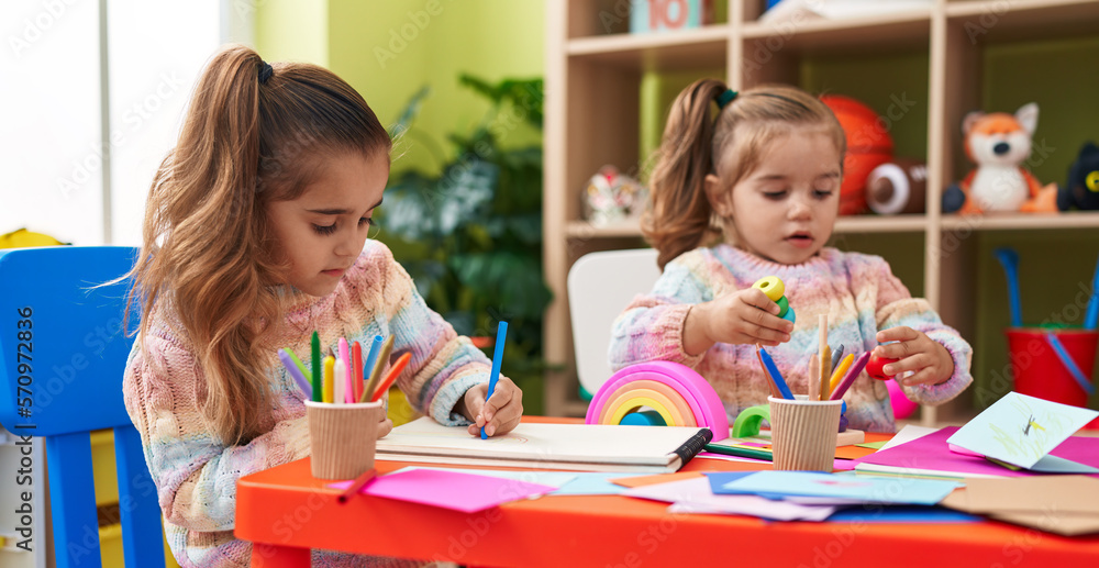 Fototapeta premium Two kids preschool students sitting on table drawing on paper at kindergarten